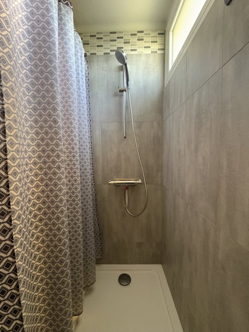 Douche moderne à la Conciergerie Maurin à Arles avec carrelage gris, rideau à motifs et pommeau de douche cascade