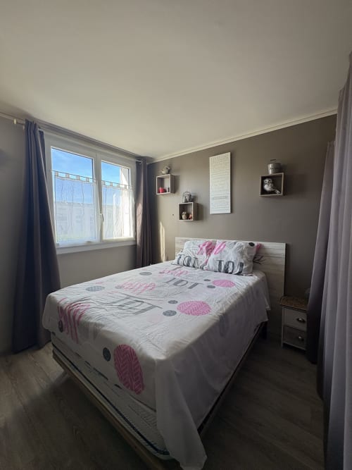 Chambre moderne à la Conciergerie Maurin à Arles avec lit queen-size, murs taupe, étagères flottantes et grandes fenêtres sur la ville