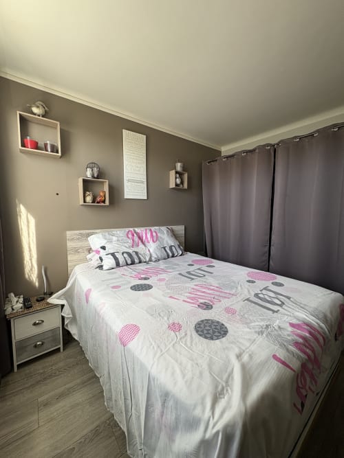 Chambre moderne à la Conciergerie Maurin à Arles avec lit queen, literie rose et grise, étagères murales et rideaux foncés