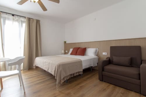 Dormitorio luminoso en El Sol II Tossa de Mar con cama, sofá marrón, suelos de madera y balcón con vistas a la ciudad