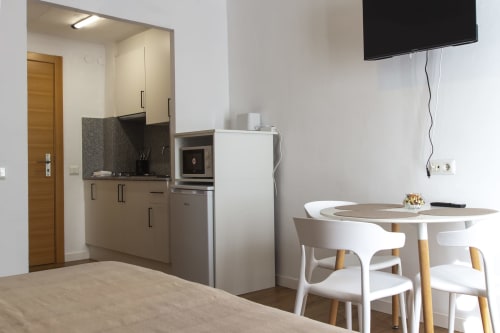 Kitchenette y comedor modernos en loft del hotel El Sol II en Tossa de Mar con sillas blancas y TV de pantalla plana