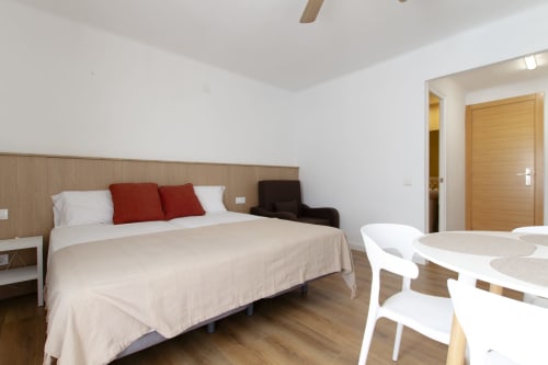 Dormitorio moderno del hotel El Sol II en Tossa de Mar con cama queen, muebles blancos y zona de comedor