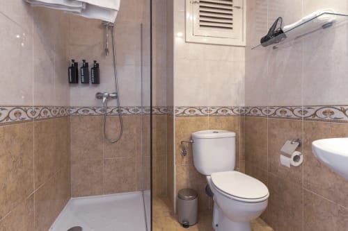 Baño moderno con ducha a ras de suelo, inodoro, lavabo y cenefa decorativa de azulejos en el hotel El Sol II de Tossa de Mar