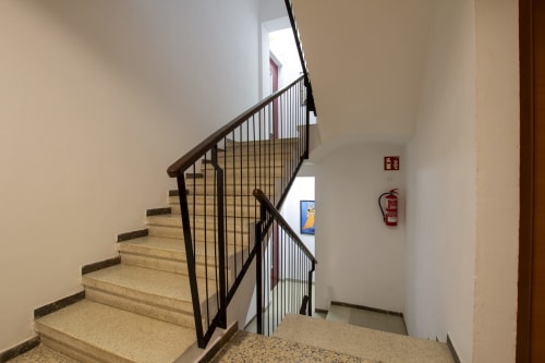 Escalera del hotel El Sol II en Tossa de Mar con barandilla metálica negra, peldaños beige y equipos de seguridad contra incendios