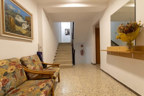 Luminoso pasillo del hotel El Sol II en Tossa de Mar con sofá floral, estante de madera, flores secas y escalera