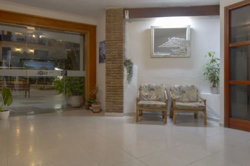 Sala de estar moderna del hotel El Sol II en Tossa de Mar, con suelos de baldosa blanca, muebles de madera, plantas y amplios espacios