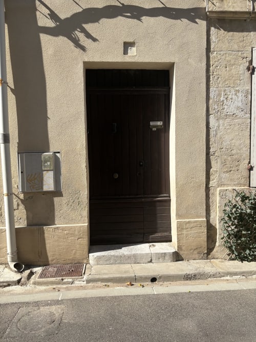 Porte noire donnant accès à une chambre de l'hôtel Conciergerie Maurin à Arles, façade en pierre beige et ombres de l'après-midi