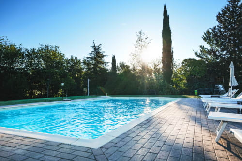 Crystal blue swimming pool at Agriturismo Marinello in Pienza, Italy, surrounded by cypress trees and loungers