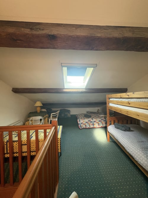 Chambre mansardée rustique à la Conciergerie Maurin, Arles avec poutres apparentes, lits en bois, fenêtre de toit et tapis vert.