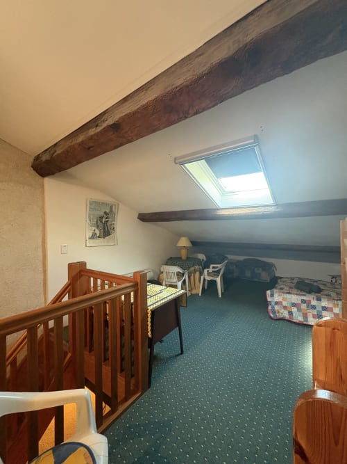 Chambre cosy sous les toits de la Conciergerie Maurin à Arles avec poutres apparentes, lucarne et mobilier rustique