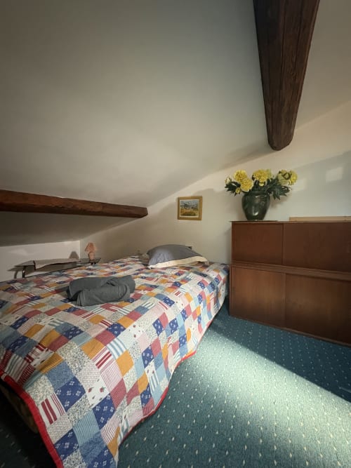 Chambre cosy sous les combles à la Conciergerie Maurin à Arles avec courtepointe patchwork, poutres en bois et fleurs jaunes