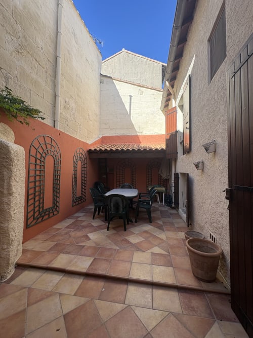 Cour intérieure de la Conciergerie Maurin à Arles avec carrelage en terre cuite, mur peint en rouge, table à manger et architecture en pierre.