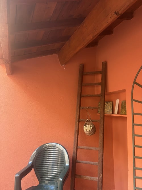 Chambre rustique à la Conciergerie Maurin à Arles avec murs orangés, poutres bois, échelle vintage et décoration traditionnelle.