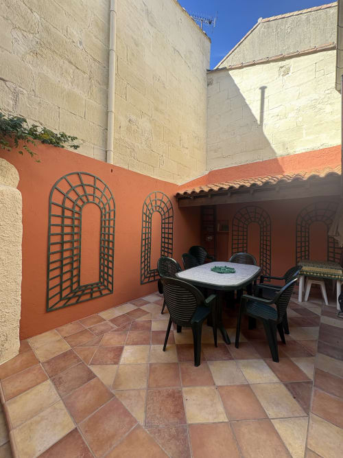 Terrasse de la Conciergerie Maurin à Arles avec murs rouges, trompe-l'œil en arche murale, table et chaises de salle à manger