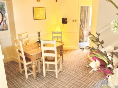 Bright yellow dining area in The Usk apartment at Brecon guesthouse with wooden chairs, potted plants, and fresh flowers