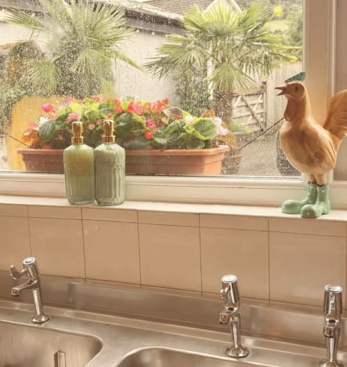 Bathroom windowsill at Usk Guest house with decorative bottles, pink flowers, and rooster figurine overlooking Brecon