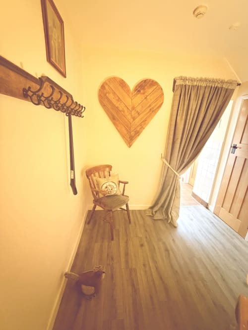 Hallway at The Usk Guest House in Brecon with wooden heart wall art, chair, cream curtains, and hardwood flooring