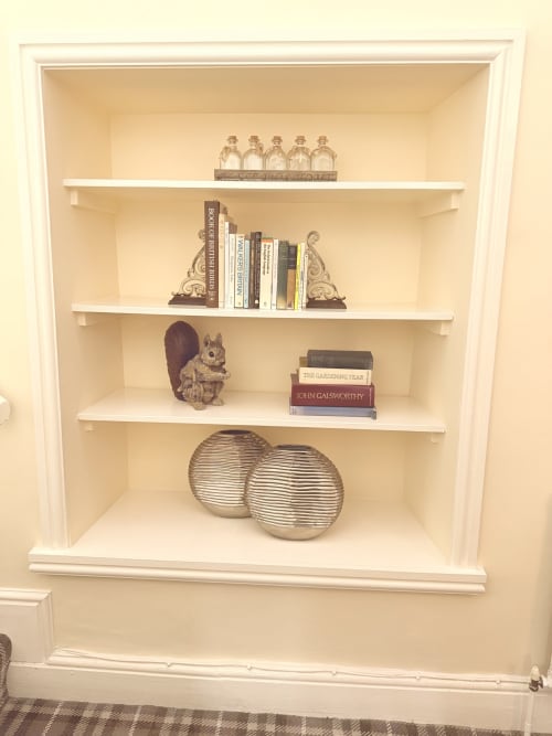 Built-in white shelving unit displaying decorative items, books, bottles, and metallic spheres in The Usk Guest House