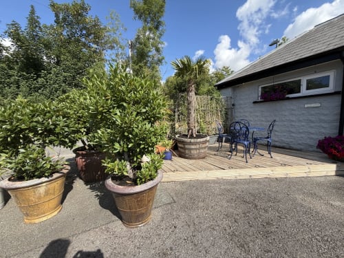 The Usk Guest House courtyard in Brecon with potted plants, wooden deck, seating area, and gray stone building under blue sky