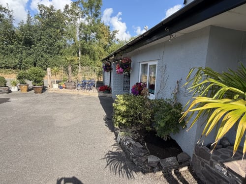 The Usk Guest House courtyard in Brecon with patio seating, flowering hanging baskets, potted plants, and mountain views