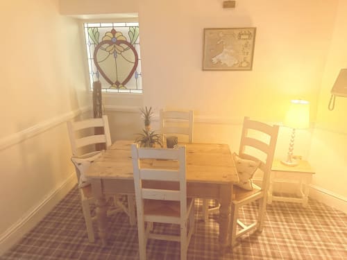 Cozy dining room at The Usk Guest house in Brecon with wooden table, ladder-back chairs, and stained glass window, bathed in