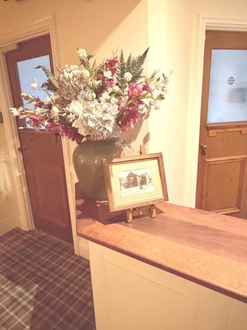 Elegant hallway at The Usk Guest House in Brecon displaying dried flowers in vase, framed artwork, and wooden doors leading