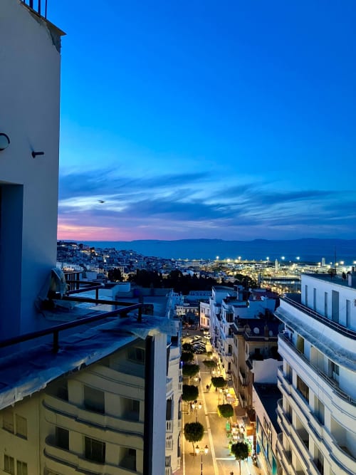 Terrasse sur le toit de SAMYA au crépuscule surplombant les rues illuminées de Tanger, la baie et les montagnes sous le ciel du soir