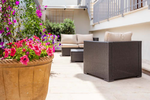 Splendido patio dell'Otranto Oasis con fiori rosa vivaci in vaso di terracotta, mobili in rattan e balcone moderno