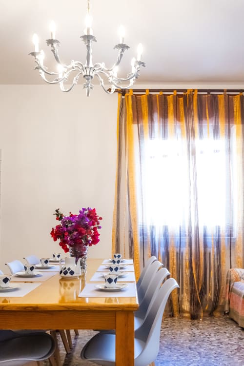 Elegante sala da pranzo dell'Otranto Oasis con lampadario, tavolo in legno, sedie bianche, fiori rossi e tende a righe dorate