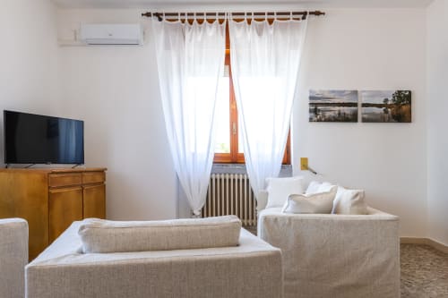 Luminosa sala d'arredo con divani beige, mobiletto TV in legno, tende bianche e paesaggi all'appartamento Otranto Oasis,