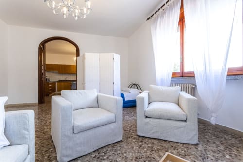Ampio soggiorno nell'appartamento Oasis di Otranto con poltroncine color crema, finestre luminose, angolo cottura e terracotta