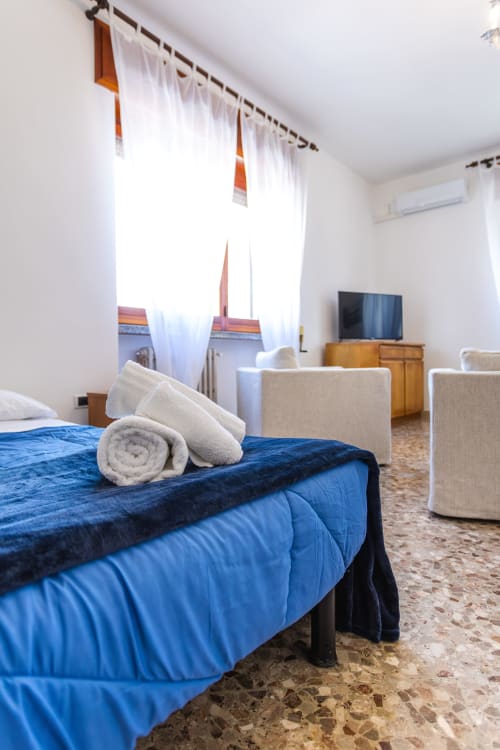 Ampia camera da letto presso l'Otranto Oasis con biancheria blu, asciugamani arrotolati, tende bianche, TV e arredi moderni a Otranto