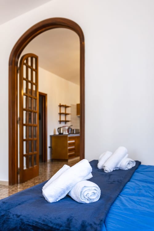 Asciugamani bianchi arrotolati sul letto blu dell'appartamento di Otranto con porta ad arco verso la cucina