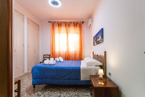 Camera luminosa dell'appartamento di Otranto con coperta blu, testata in rattan, tende arancioni e comfort moderni