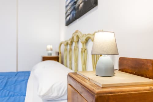 Camera da letto moderna nell'appartamento di Otranto con lampada da tavolo bianca, mobili in legno e biancheria blu vicino alla testata.