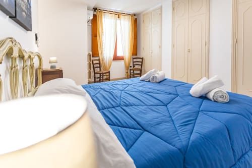 Camera spaziosa presso Otranto Oasis con piumone blu, cuscini bianchi, struttura letto dorata e tende dorate