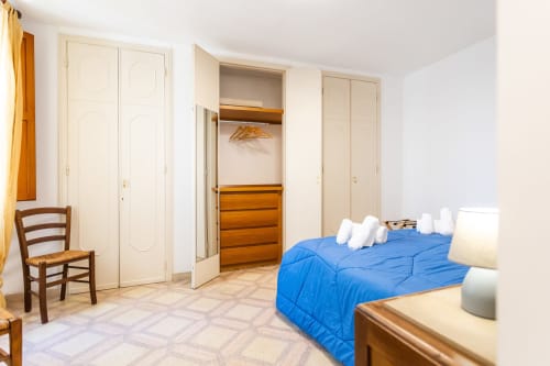 Ampia camera da letto presso Otranto Oasis con piumone blu, armadio in legno, ripostigli color crema e pavimento piastrellato a Otranto