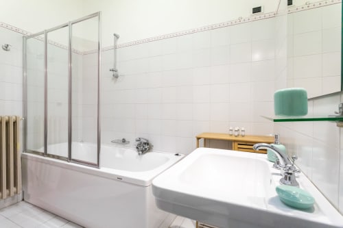 Moderno bagno nell'appartamento Otranto Oasis con piastrelle bianche, vasca, cabina doccia e lavabo con dettagli verdi.