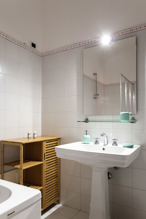 Bagno moderno con lavabo su colonna, specchio, ripiano in vetro, porta in legno per sauna e piastrelle bianche all'Oasis di Otranto.