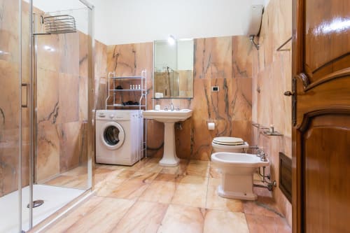 Bagno spazioso dell'Oasis di Otranto con piastrelle in marmo, doccia, WC, bidet, lavabo su piedistallo, lavatrice e