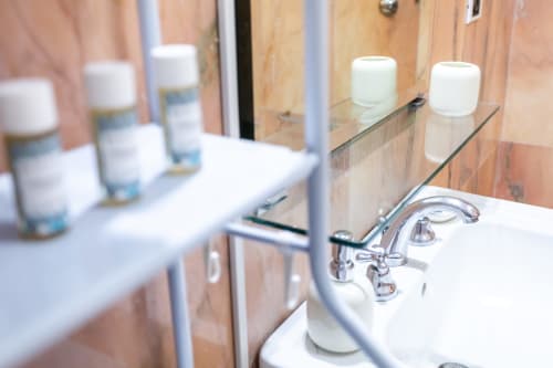 Bagno moderno con flaconi bianchi su mensola, specchio e rubinetto cromato presso l'appartamento Otranto Oasis