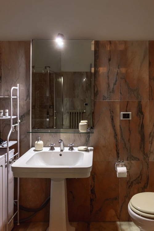Bagno moderno con lavabo su colonna, pareti in marmo e specchio illuminato nell'appartamento Otranto Oasis, Otranto Italia