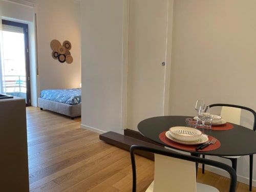 Zona pranzo moderna nell'appartamento di Palermo con tavolo nero, dettagli di mise en place, pavimenti in legno e camera da letto visibile