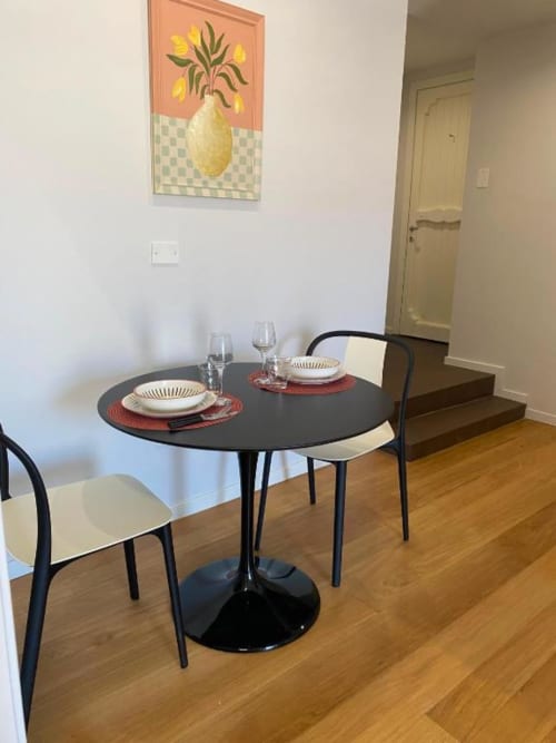 Elegante sala da pranzo in appartamento Bnb a Palermo con tavolo rotondo nero, sedie color crema, coperto tavola e quadro con fiori gialli