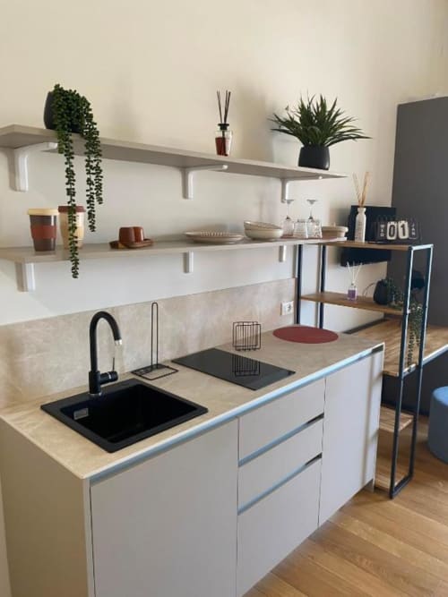 Cucina moderna nell'appartamento di Palermo con mobili bianchi, lavello nero, piani in legno chiaro, mensole galleggianti con piante