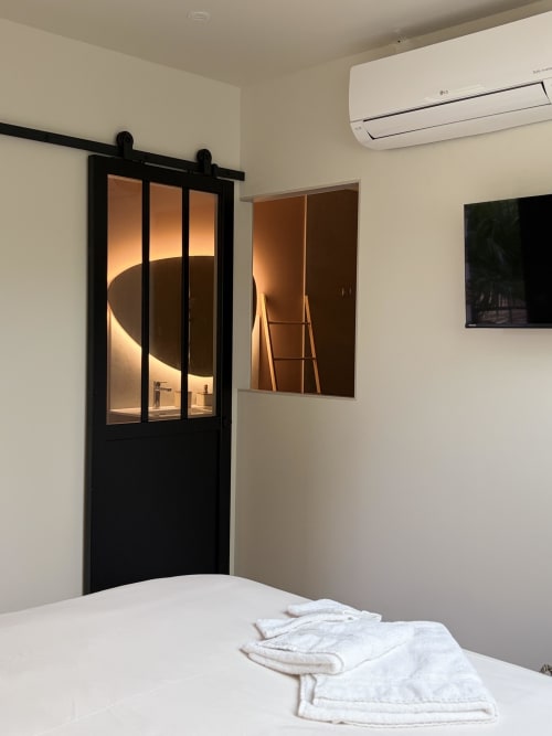 Chambre moderne à La cour des Agapanthes avec porte grange noire, literie blanche, climatisation et accès salle de bain