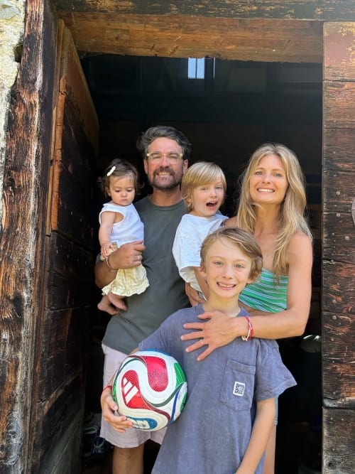Happy family of five posing at Les Chalets d'Arrens hostel entrance in Arrens Marsous, holding soccer ball