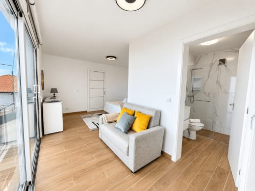 Modern studio at Sunshine House 85, Ribeira Brava: beige sofa with pillows, bed, ensuite bathroom, wooden floors, sea view