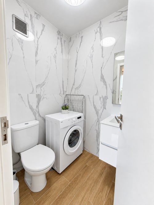 Modern bathroom with marble walls, white toilet, front-load washer, and wooden flooring in Sunshine House 85 villa at Check