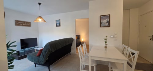 Salon moderne de l'appartement NN Patrimoine Douvaine avec canapé, table à manger, télévision et luminaires suspendus